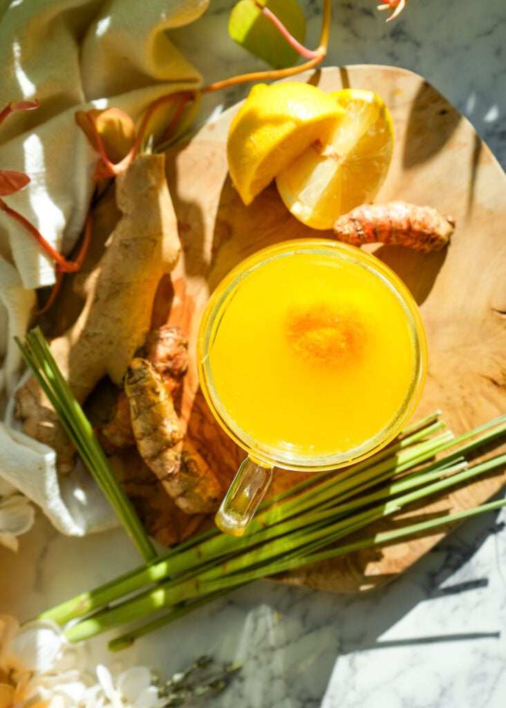 Close-up of vibrant yellow tea bomb mixture in a measuring cup surrounded by fresh ingredients.