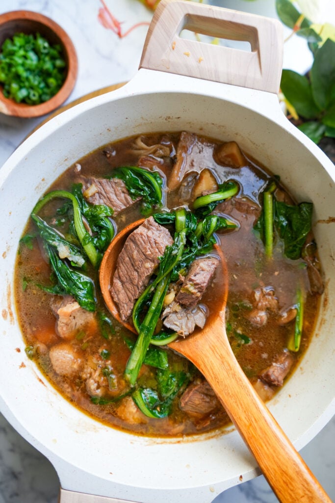 ginger beef soup in a large pot with wooden spoon