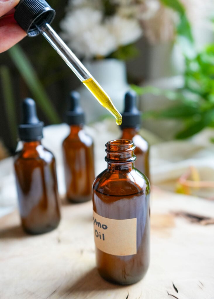 A dropper filled with golden oregano oil being held above an amber bottle.