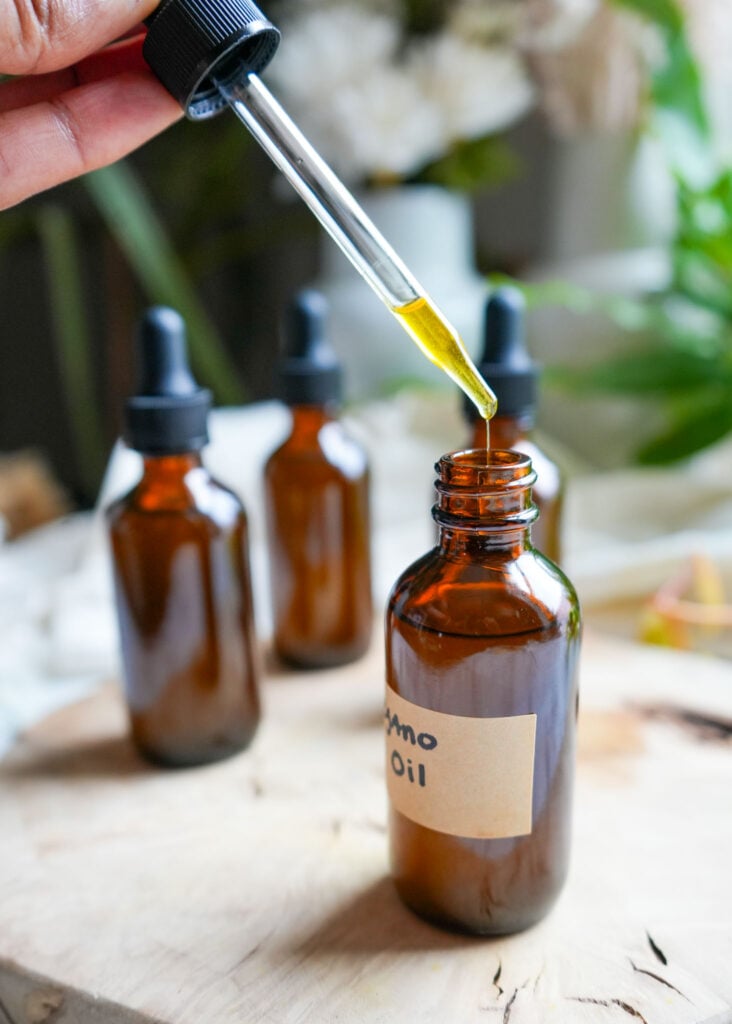 A close-up of golden oregano oil dripping from a dropper into an amber glass bottle.