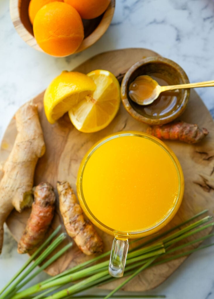 A cozy setup featuring a warm lemon turmeric tea with fresh ginger, turmeric, lemongrass, and honey on a wooden cutting board.