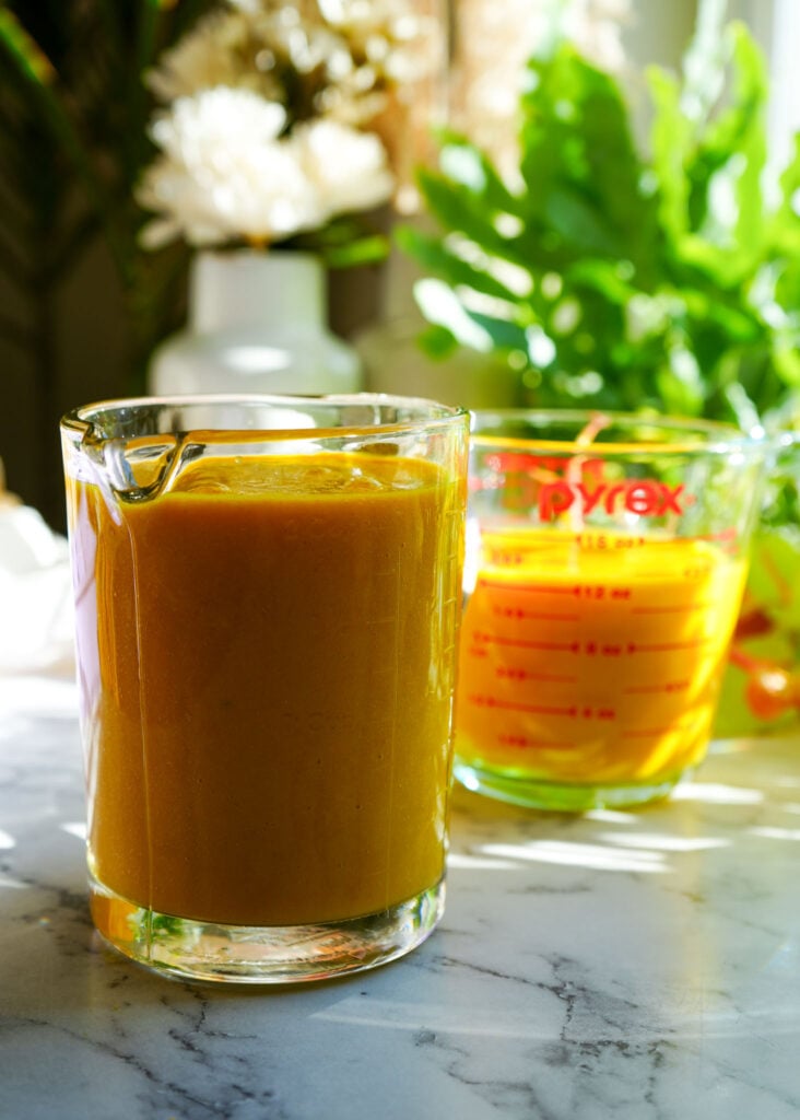 Two measuring cups filled with a golden turmeric and lemon mixture, placed on a marble countertop.