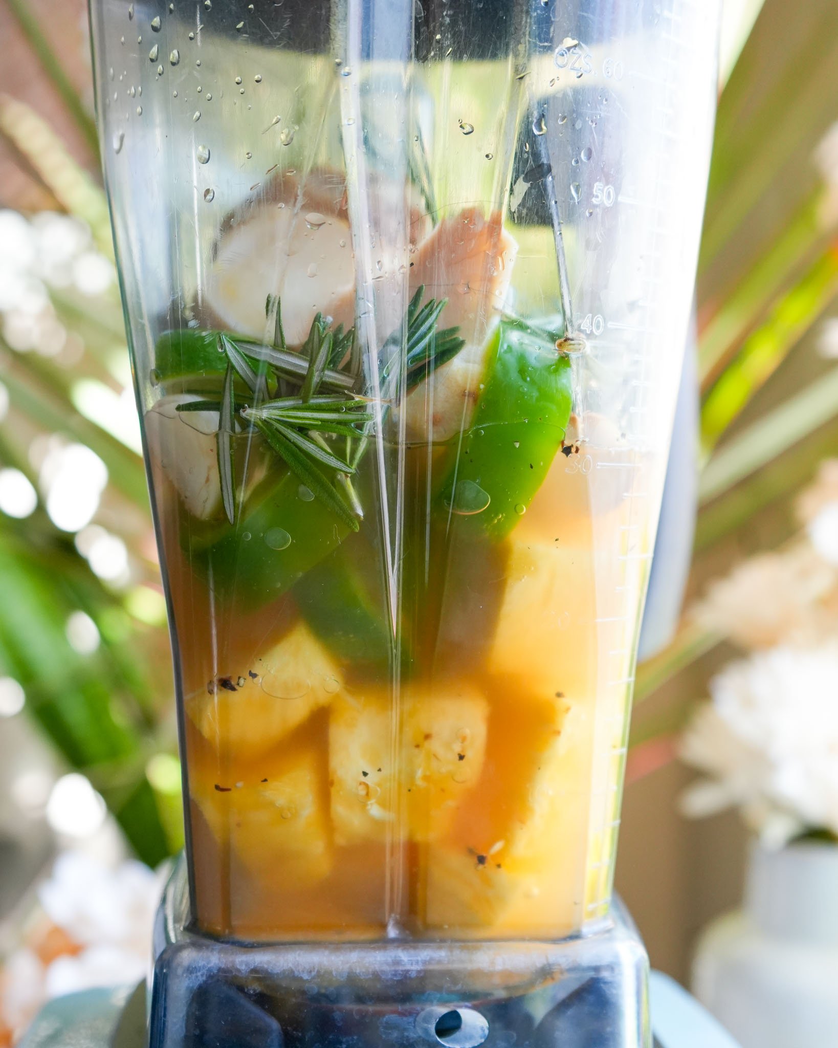 A blender filled with vibrant ingredients like pineapple, jalapeño, and rosemary, ready to be blended for quick fire cider.