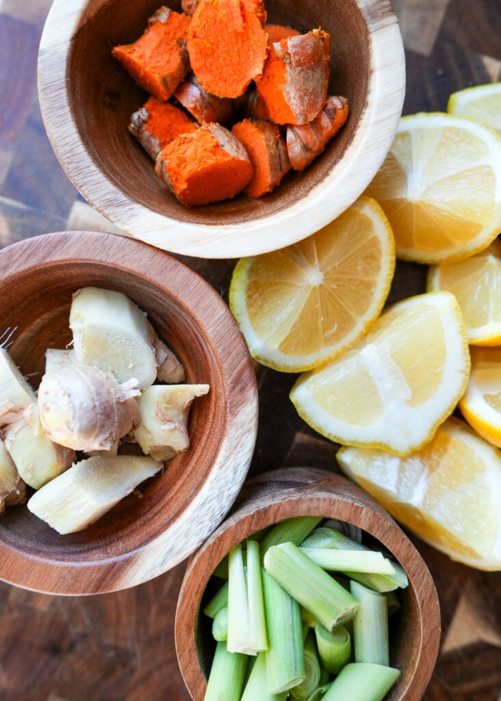 Fresh ingredients for frozen tea bombs including lemons, ginger, turmeric, and lemongrass, neatly arranged in wooden bowls.