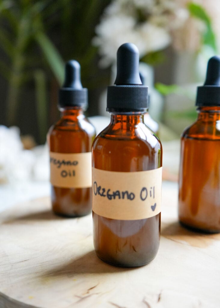 Amber glass bottles labeled "Oregano Oil" on a wooden surface with a blurred natural background.