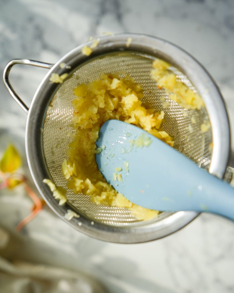 pressing ginger through a fine mesh strainer with a rubber spatula