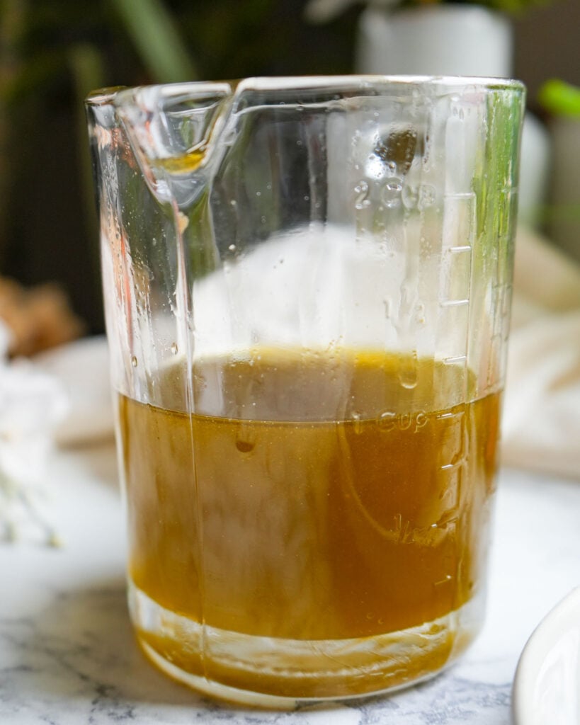 Golden oregano oil being strained through cheesecloth into a measuring cup, showing the infusion process.