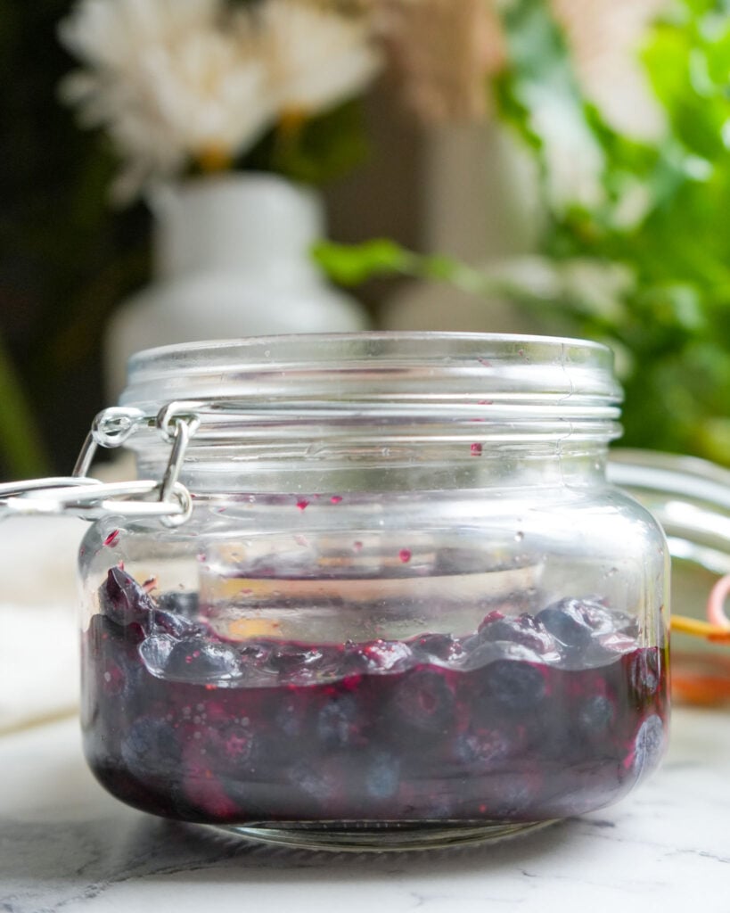 A close-up of a glass jar on day five of fermentation, showing the blueberries submerged in brine with bubbles forming.