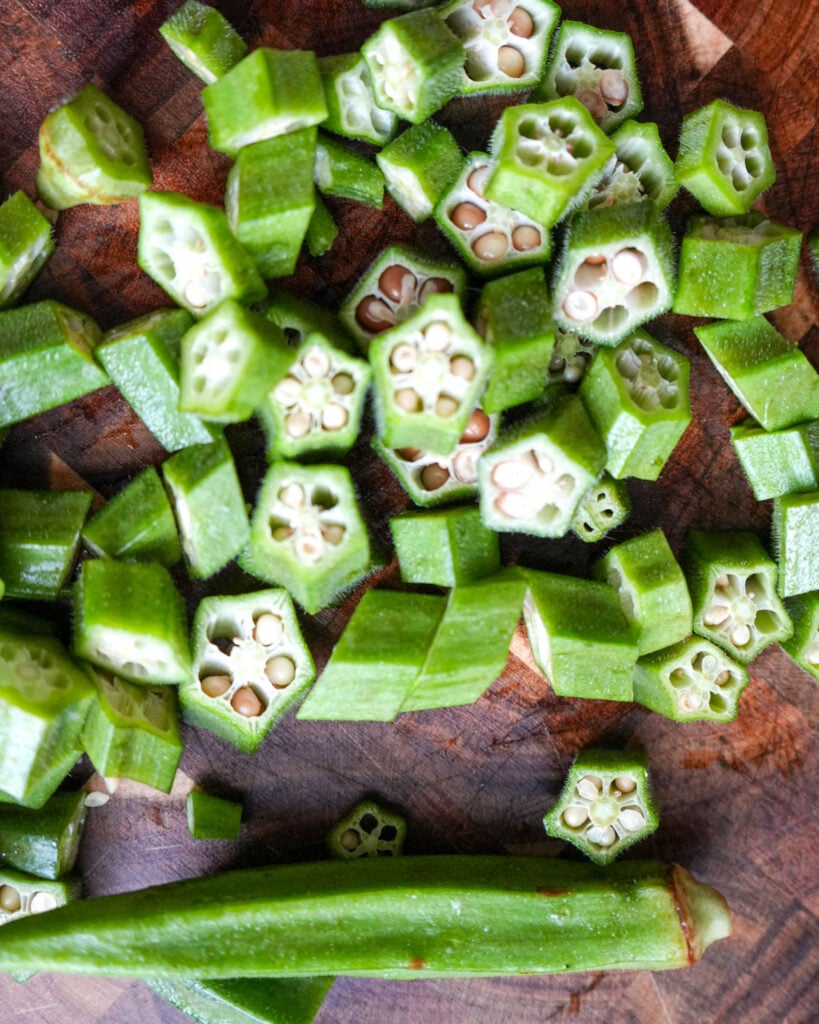 A close-up of freshly chopped okra pieces on a wooden cutting board, showcasing their bright green color and distinct seed pattern.