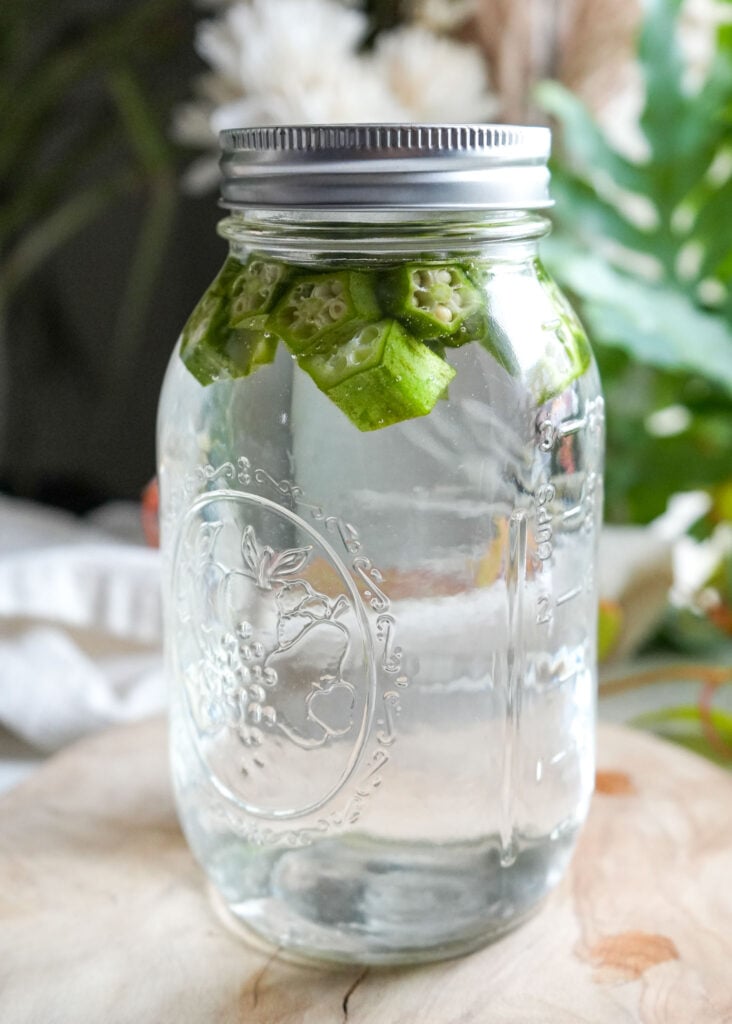 A sealed mason jar filled with plain okra water, showing okra pieces floating at the top, set against a neutral background with soft lighting.