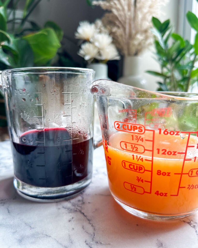 a measuring cup with hibiscus liquid on the left and a measuring cup with fresh citrus juice on the right