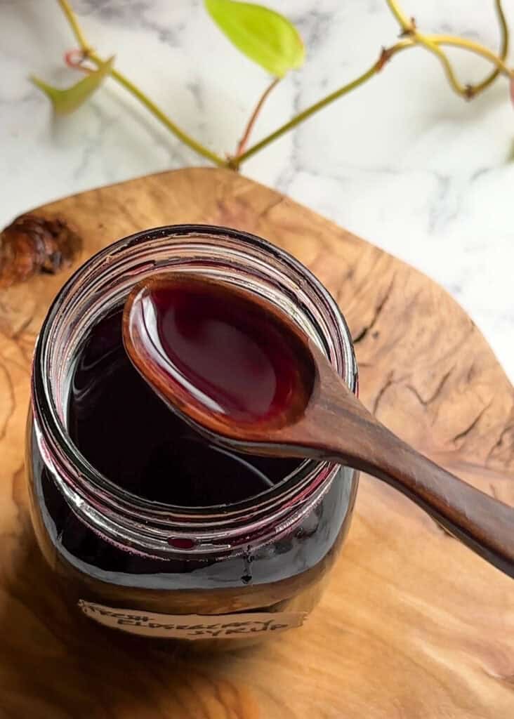 homemade elderberry syrup in a wooden spoon