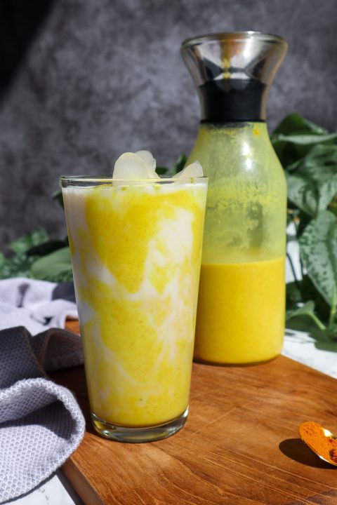 iced golden milk in a tall glass with a carafe of golden milk behind the glass