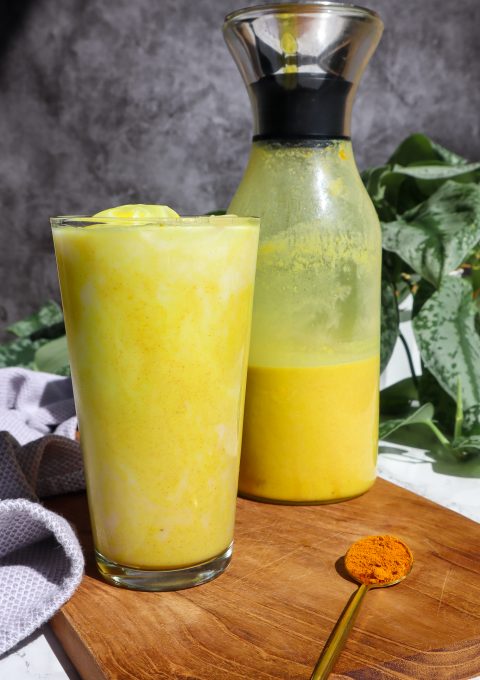 iced golden milk in a tall glass with a carafe of golden milk behind the glass